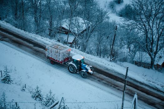 Aerial view of a tractor pulling a loaded trailer down a snowy road in Şavşat, Artvin, Türkiye.