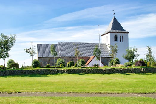 Beautiful view of Mabjerg Church in Denmark, surrounded by lush greenery and clear blue skies.