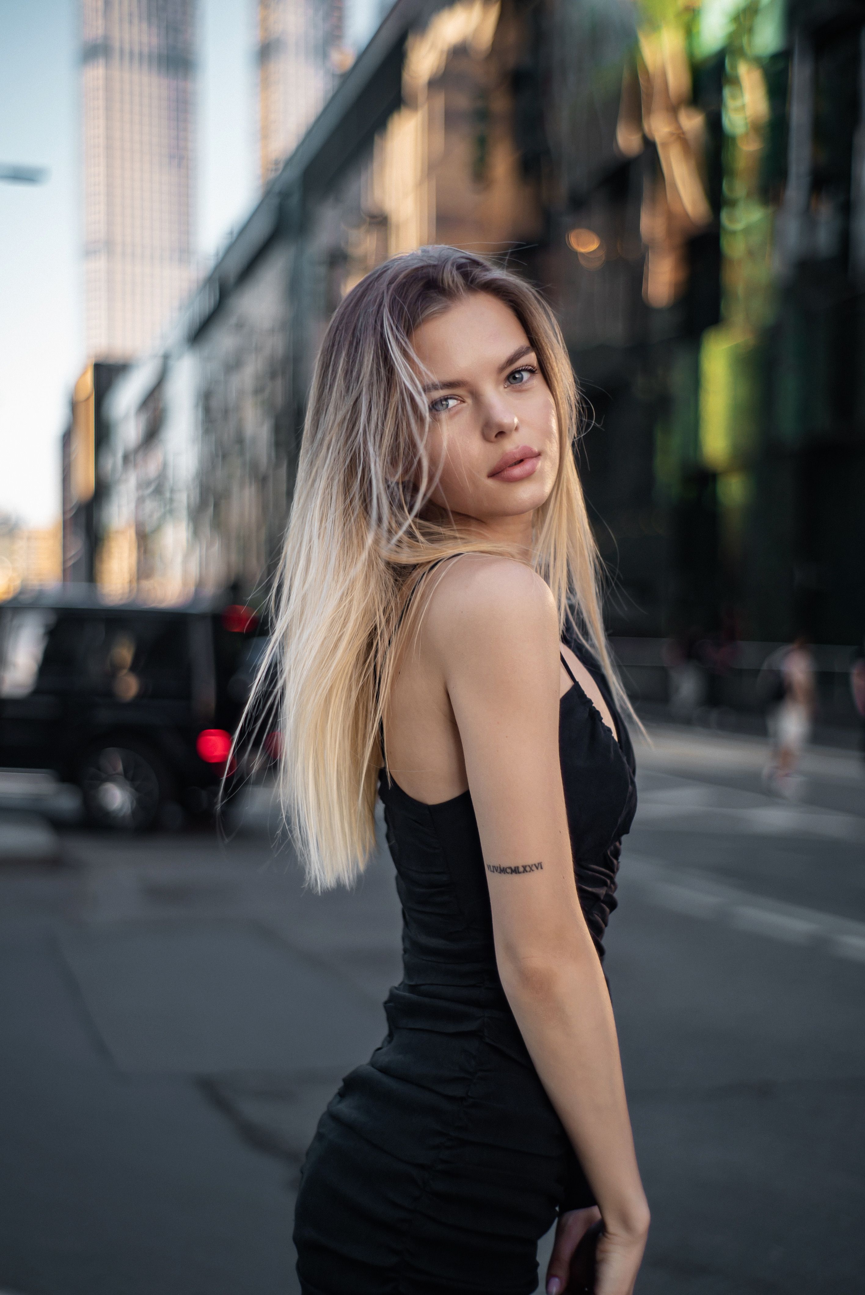 Stylish blonde woman posing confidently in a modern urban cityscape.