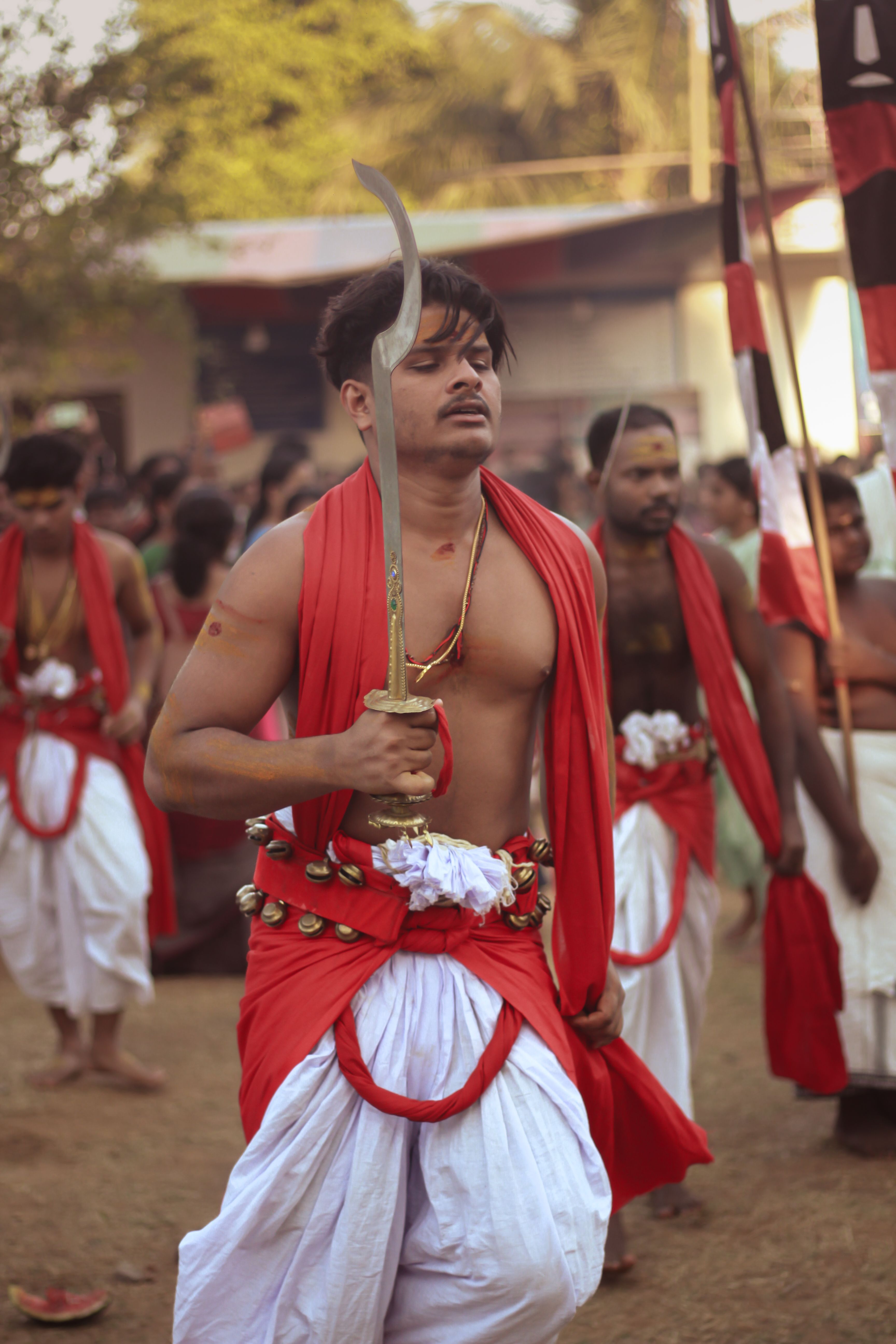 Men in vibrant attire perform traditional sword dance during a colorful Kerala festival.