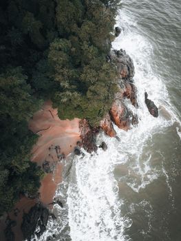 Stunning aerial shot of a rocky beach in Malaysia with lush greenery and waves crashing on the shore.