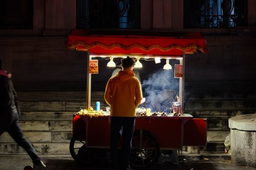 Free A street vendor stands at a well-lit cart selling food at night in an urban setting. Stock Photo