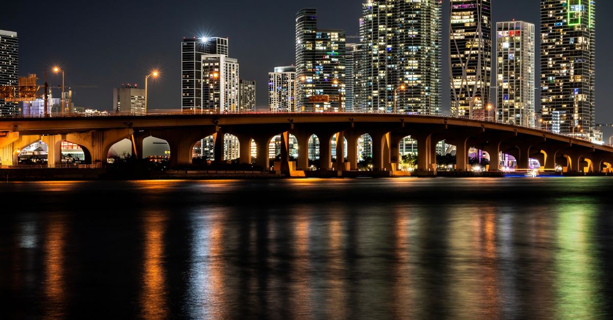 Gorgeous night view of Miami's illuminated skyline and bridge reflections on water, offering a captivating cityscape.