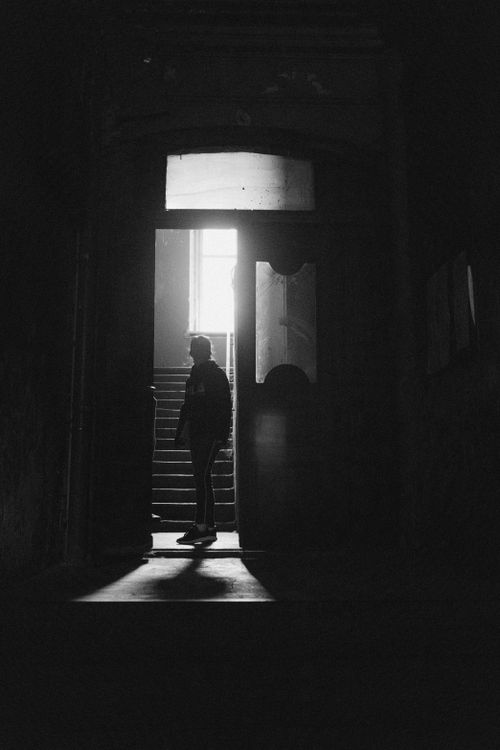 Free Moody black and white photo of a woman silhouetted in an old building's doorway, creating an eerie ambiance. Stock Photo