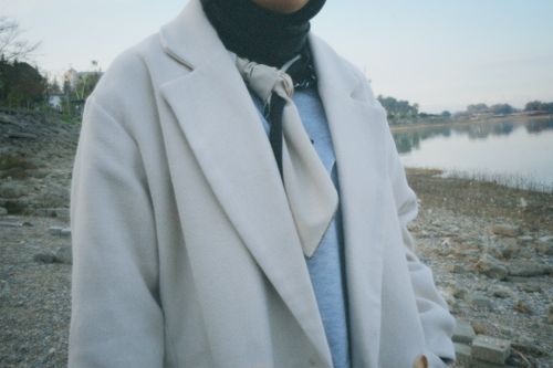 Free A woman stands by the riverbank wearing a stylish white coat, showcasing modern fashion. Stock Photo