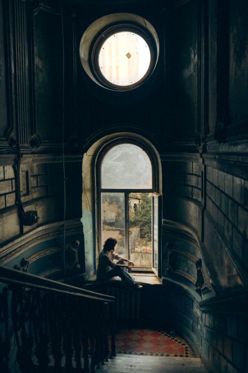 Free A person sits in silhouette by a window in a dark, historic stairwell. Stock Photo