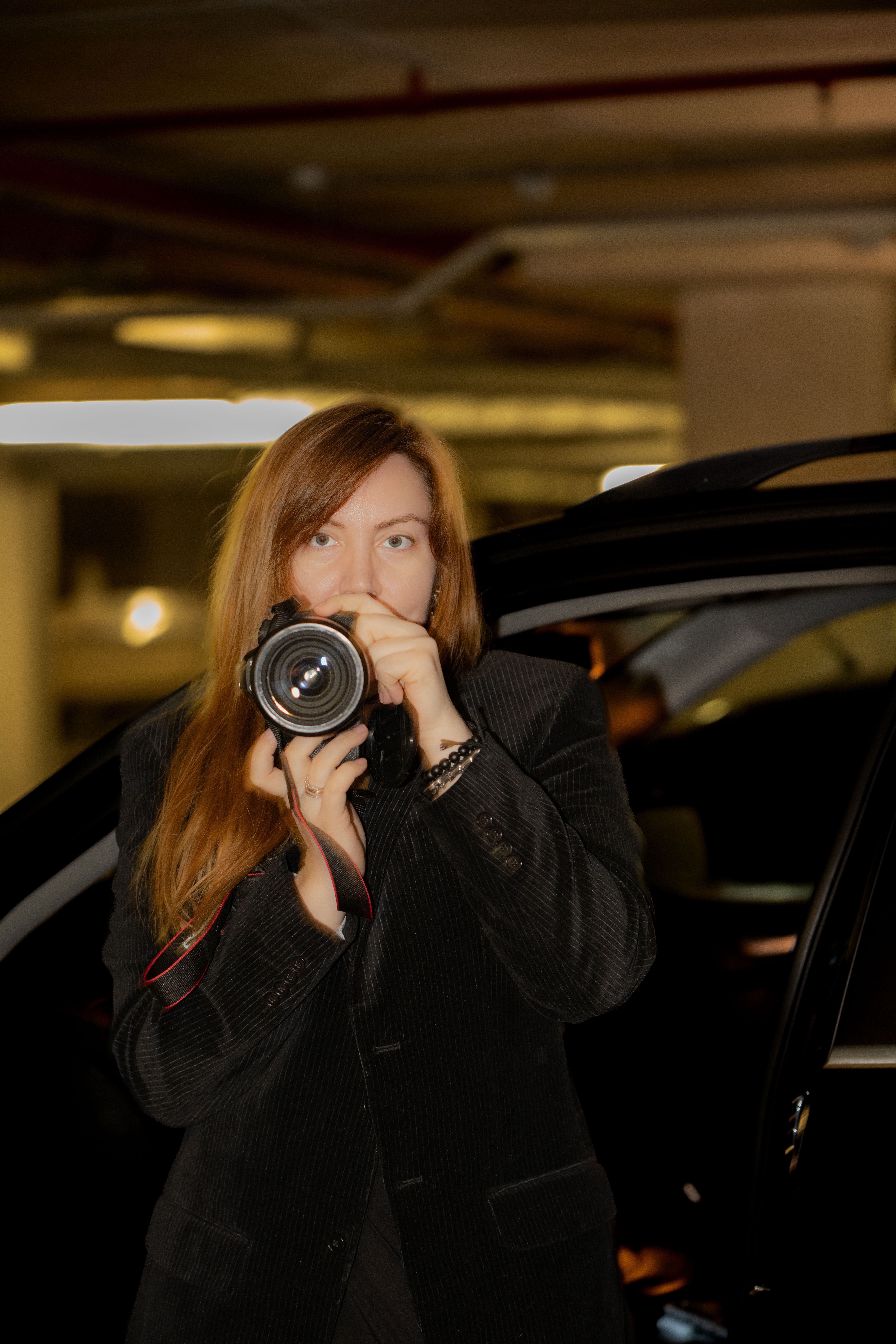 Woman with long brown hair taking pictures in an indoor parking lot.