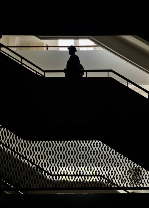 Free Dramatic silhouette of a person in a hat standing on an indoor staircase with geometric patterns. Stock Photo