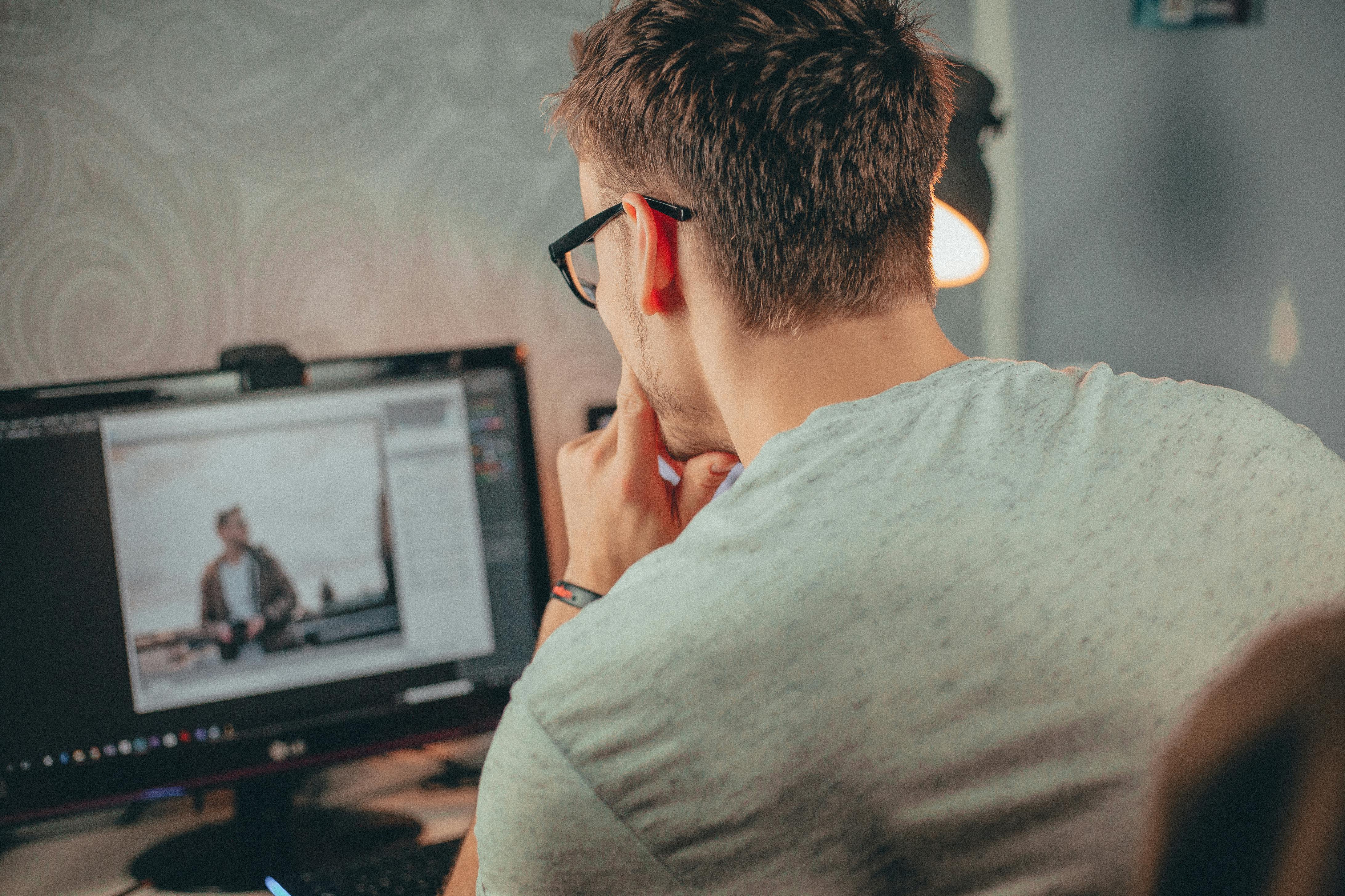 A man with glasses focused on editing a photo on his desktop computer in an office.