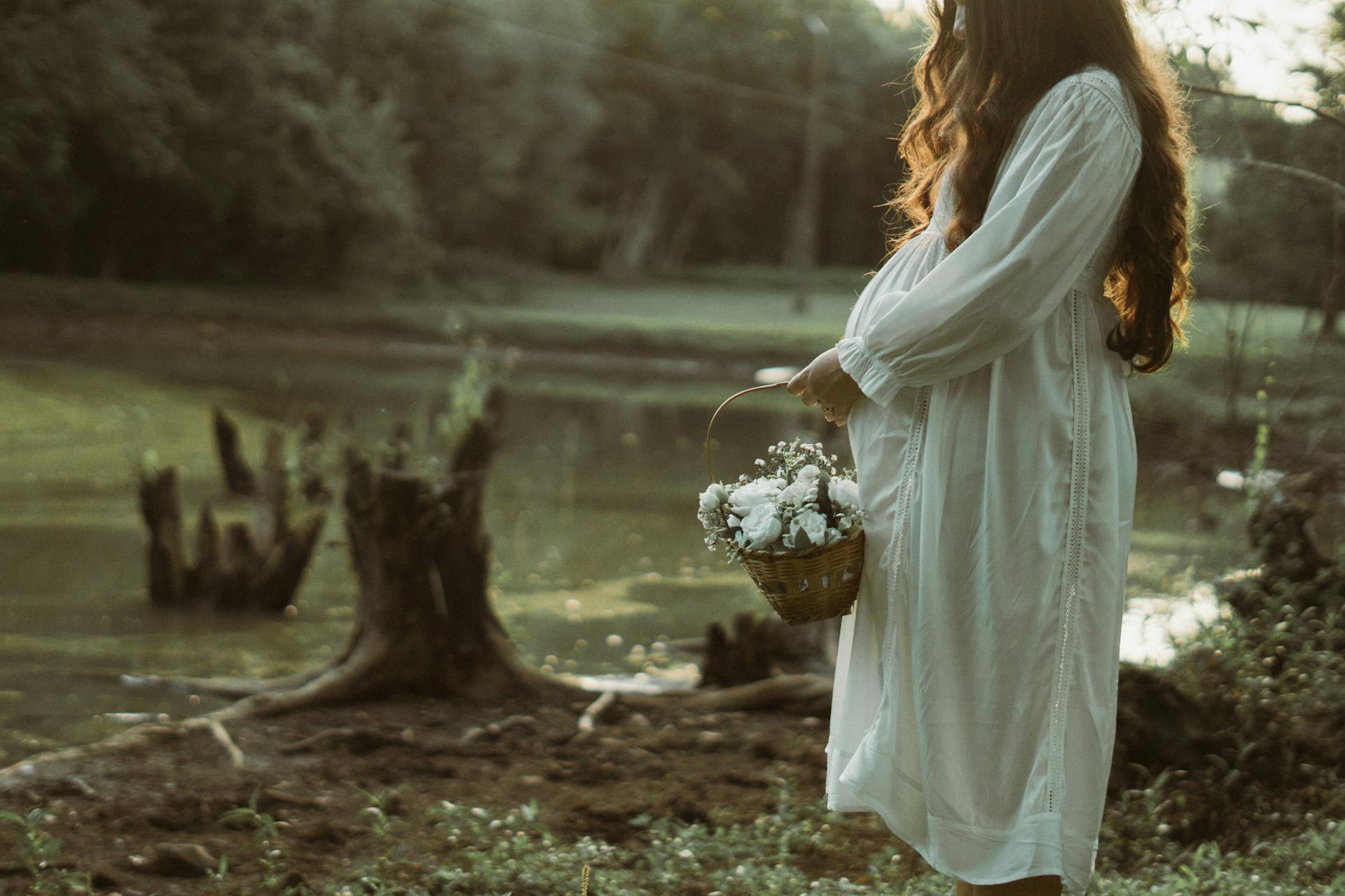 Pregnant Woman with Basket of Flowers by River in Summer