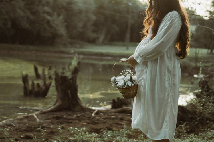 Pregnant Woman With Basket Of Flowers By River In Summer