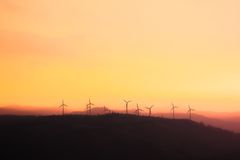 Silhouette of wind turbines at sunset, promoting sustainable energy.