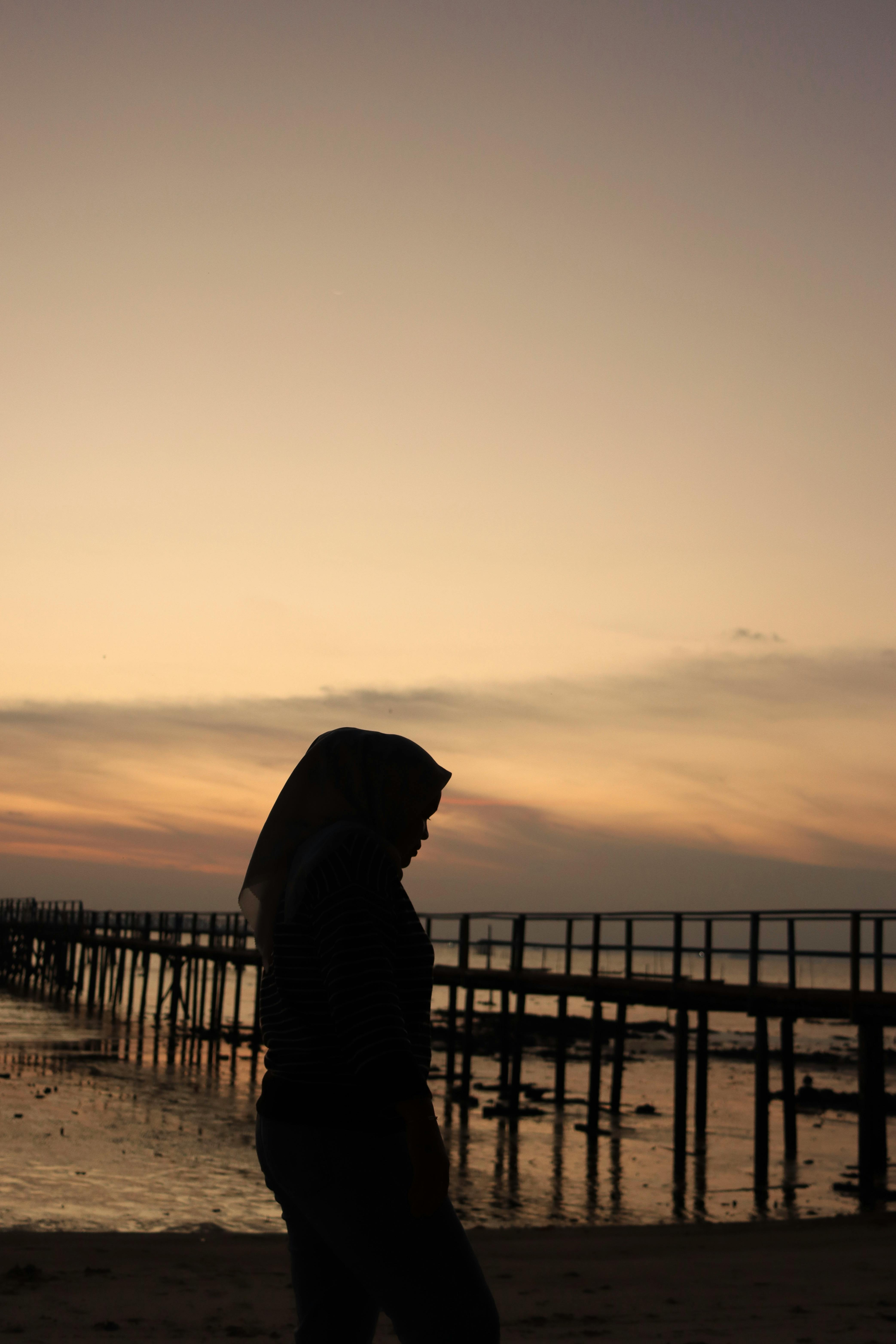 A serene silhouette of a woman walking along a pier at sunset, creating a tranquil beach scene.