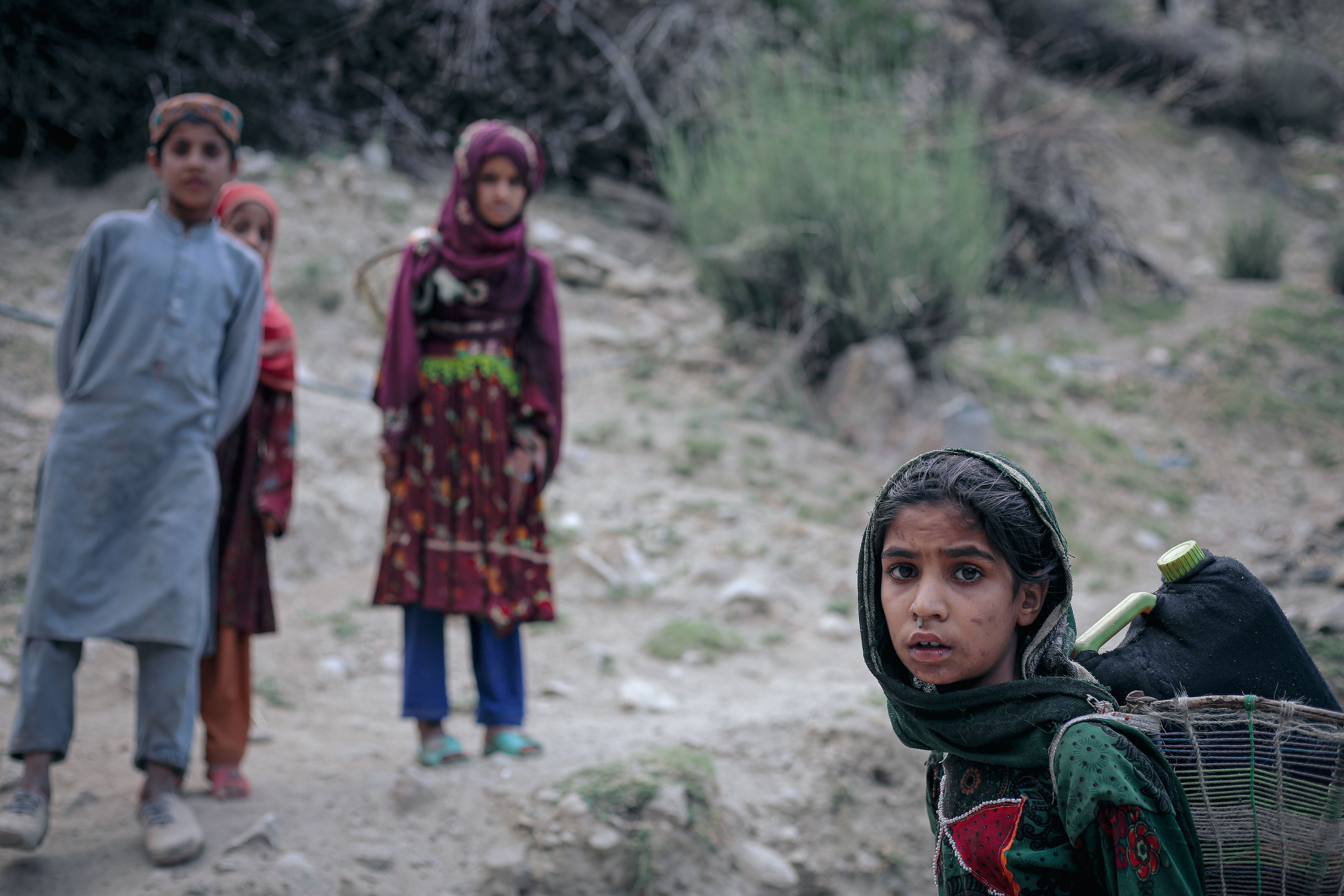 Children in a rural Afghan village carrying goods along a footpath in a hilly area.