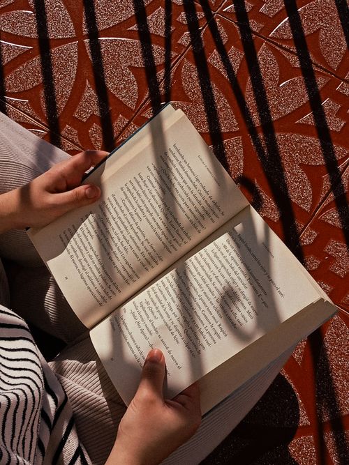 Free Hands holding a book with shadow play on a patterned surface outdoors. Stock Photo