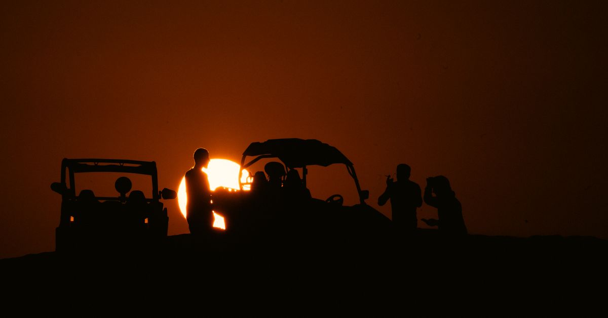 Silhouettes of people enjoying a scenic sunset in the desert of Al Wakrah, Qatar, with off-road vehi
