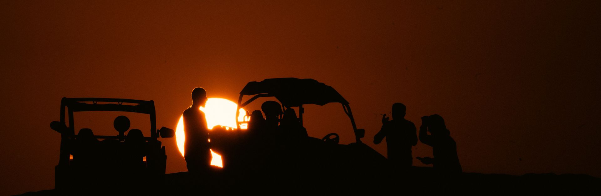 Silhouettes of people enjoying a scenic sunset in the desert of Al Wakrah, Qatar, with off-road vehi