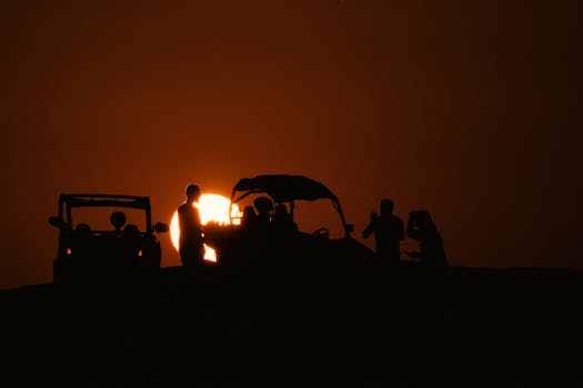 Silhouettes of people enjoying a scenic sunset in the desert of Al Wakrah, Qatar, with off-road vehicles.
