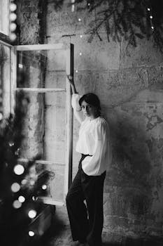 Stylish black and white portrait of a woman posing by a rustic window.