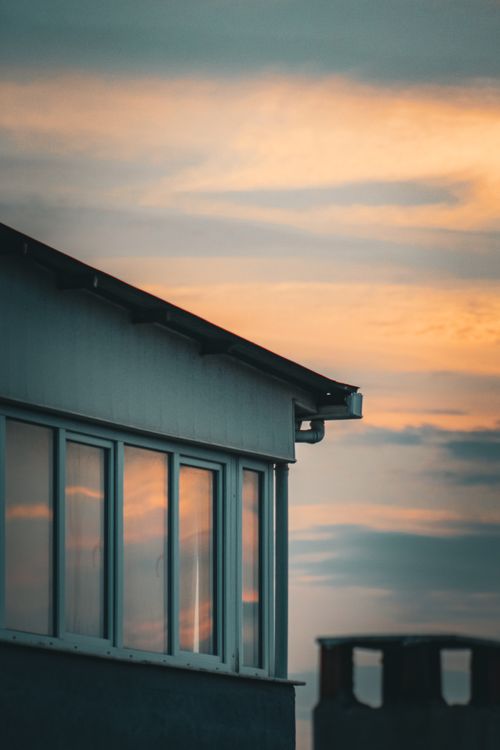 Free A serene view of a house's silhouette against a colorful sunset sky with clouds reflecting on windows. Stock Photo