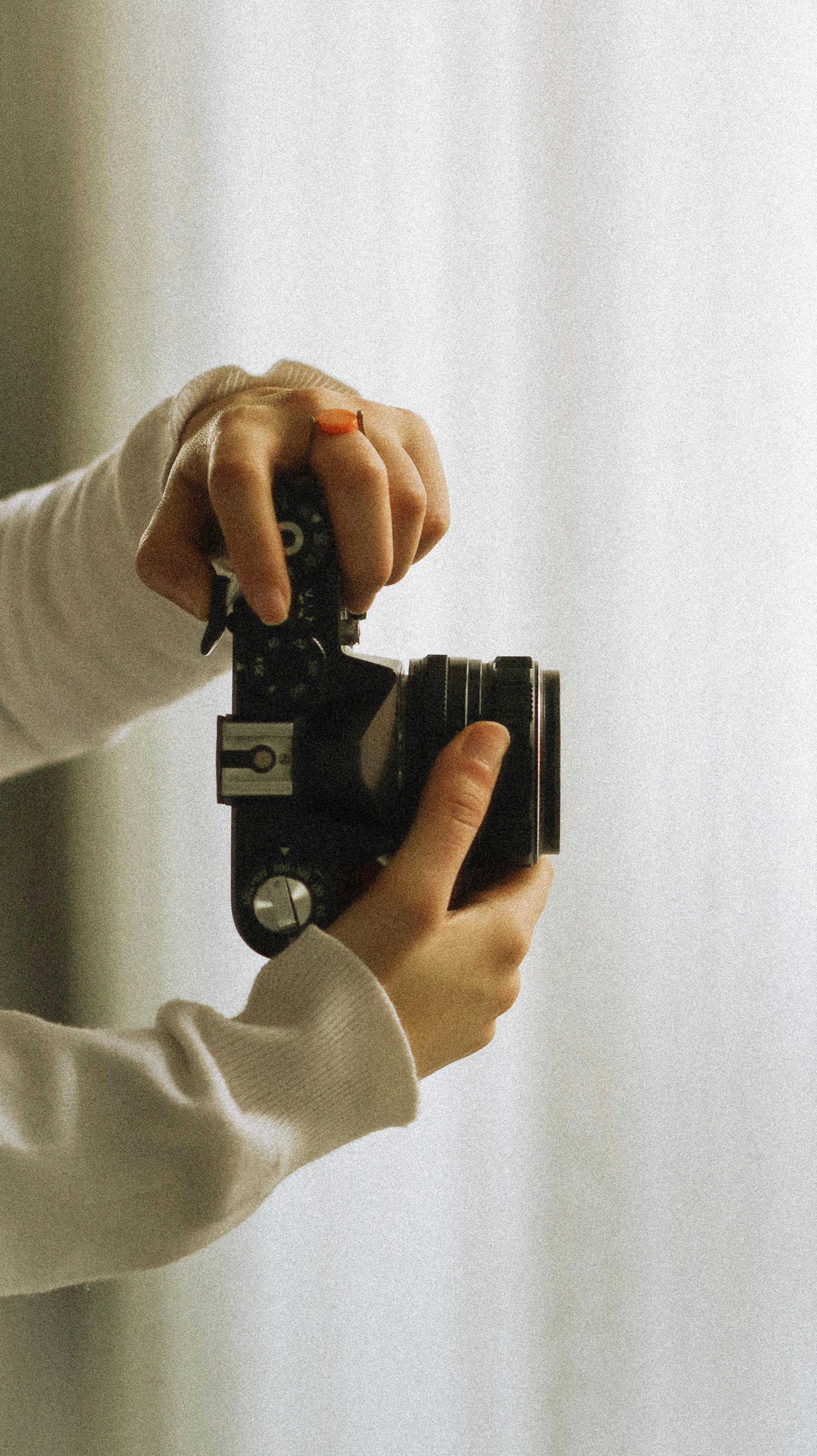 Detailed image of hands holding a vintage film camera against a light background.