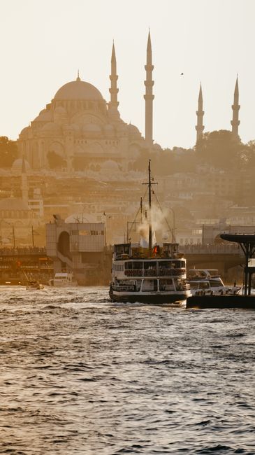 A ferry navigates the Bosphorus Strait with Istanbul's iconic mosques in the background at sunrise.