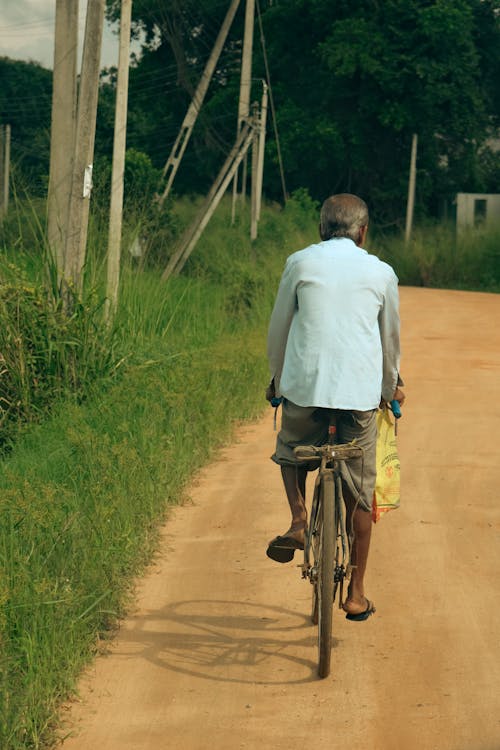 Back View of a Man Riding a Bicycle on a Sandy Road