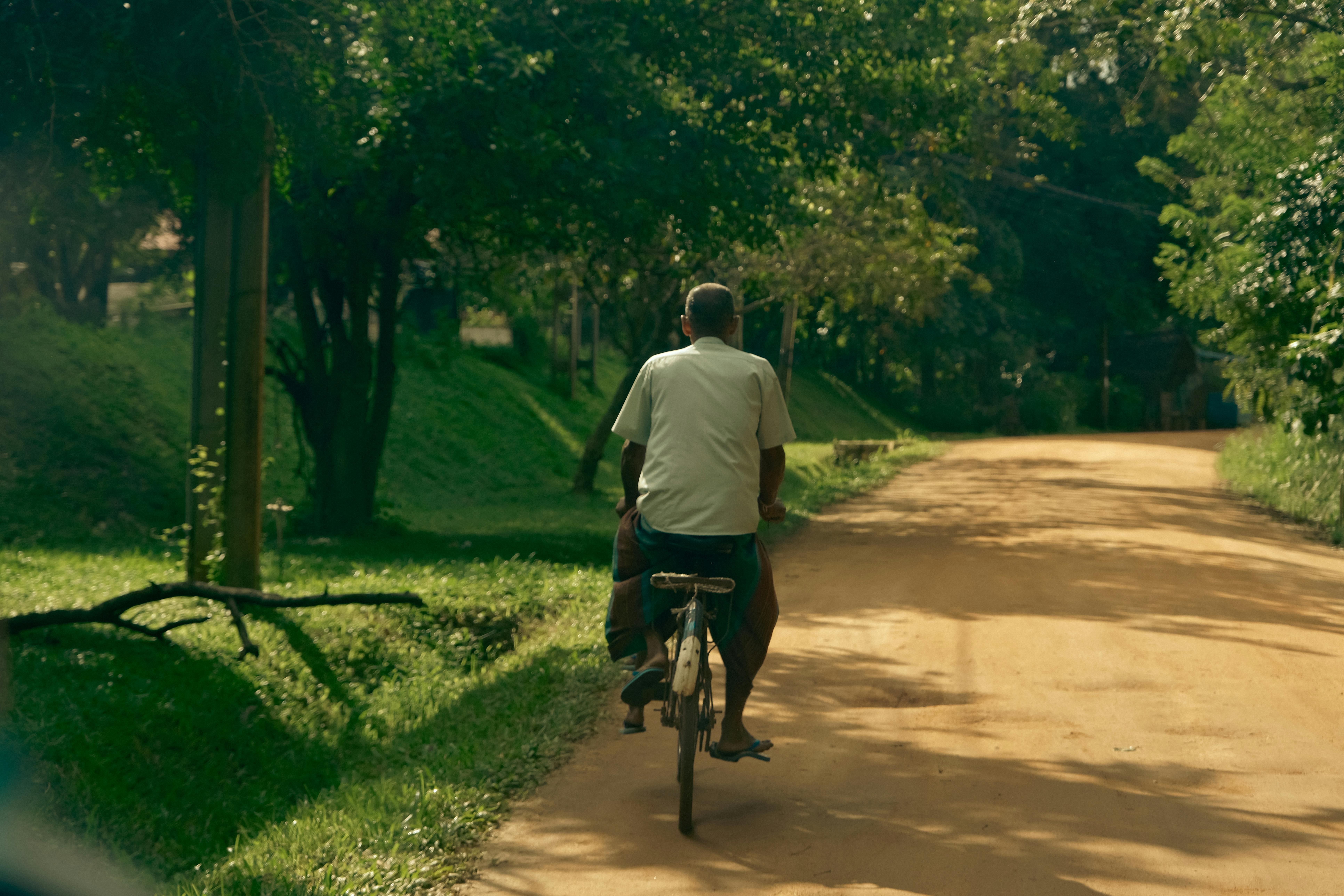 Man cycling on a serene dirt road surrounded by lush greenery — biking in Sri Lanka