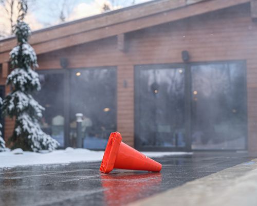 Free Red traffic cone on icy pavement in front of snowy building during winter. Stock Photo