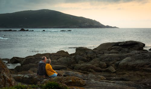 Man and Woman Sitting on Coastline and Looking at View