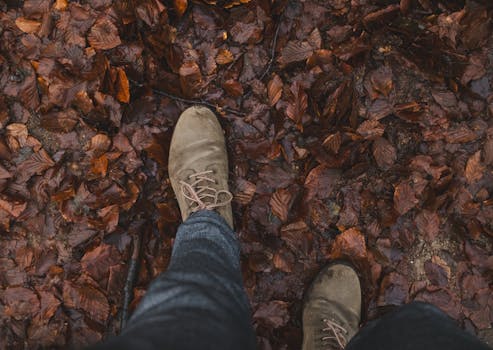 Brown leather boots stepping on autumn leaves, showcasing fall fashion outdoors.