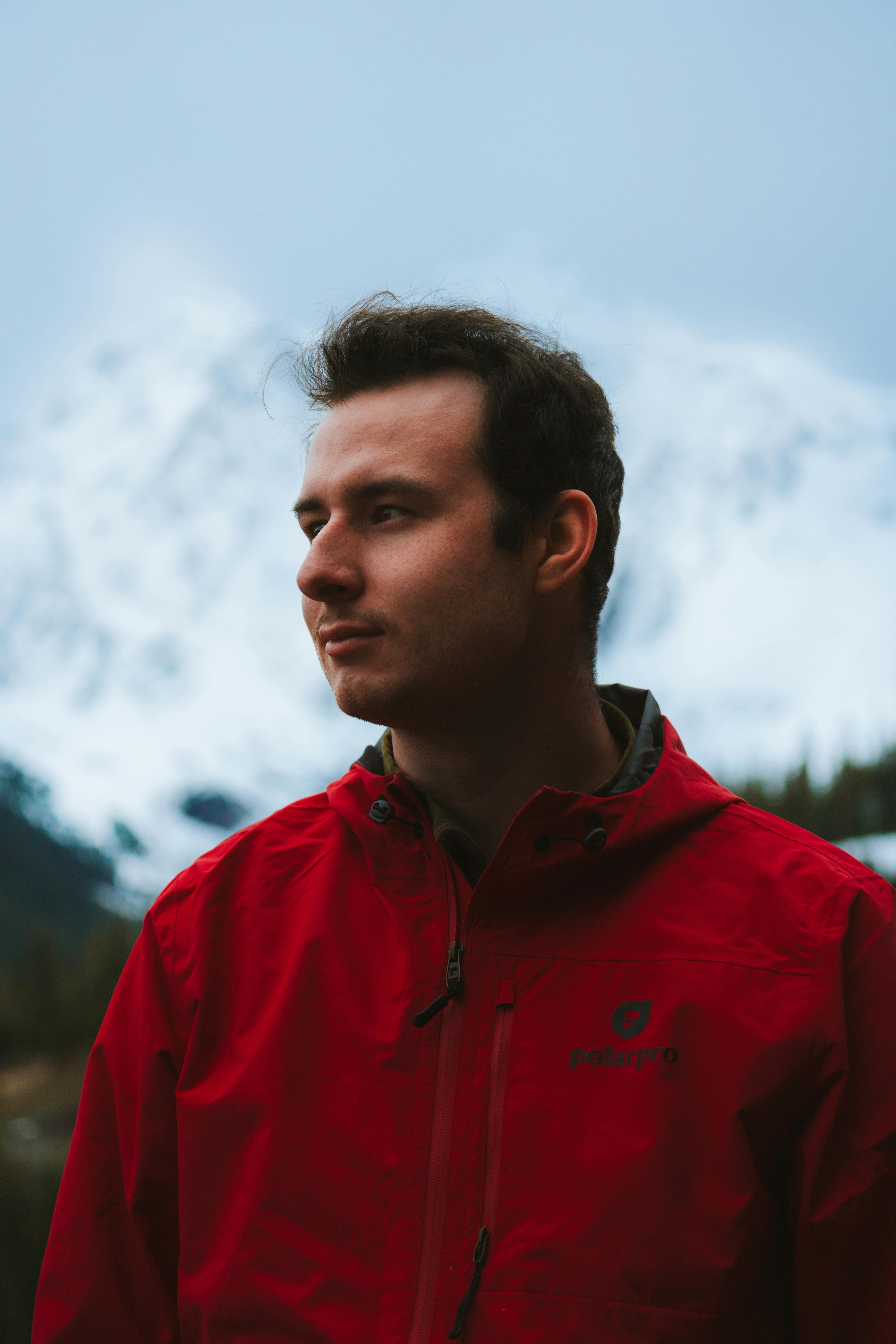 A contemplative man in a red jacket with snowy mountains in the background, depicting an adventurous spirit in nature.
