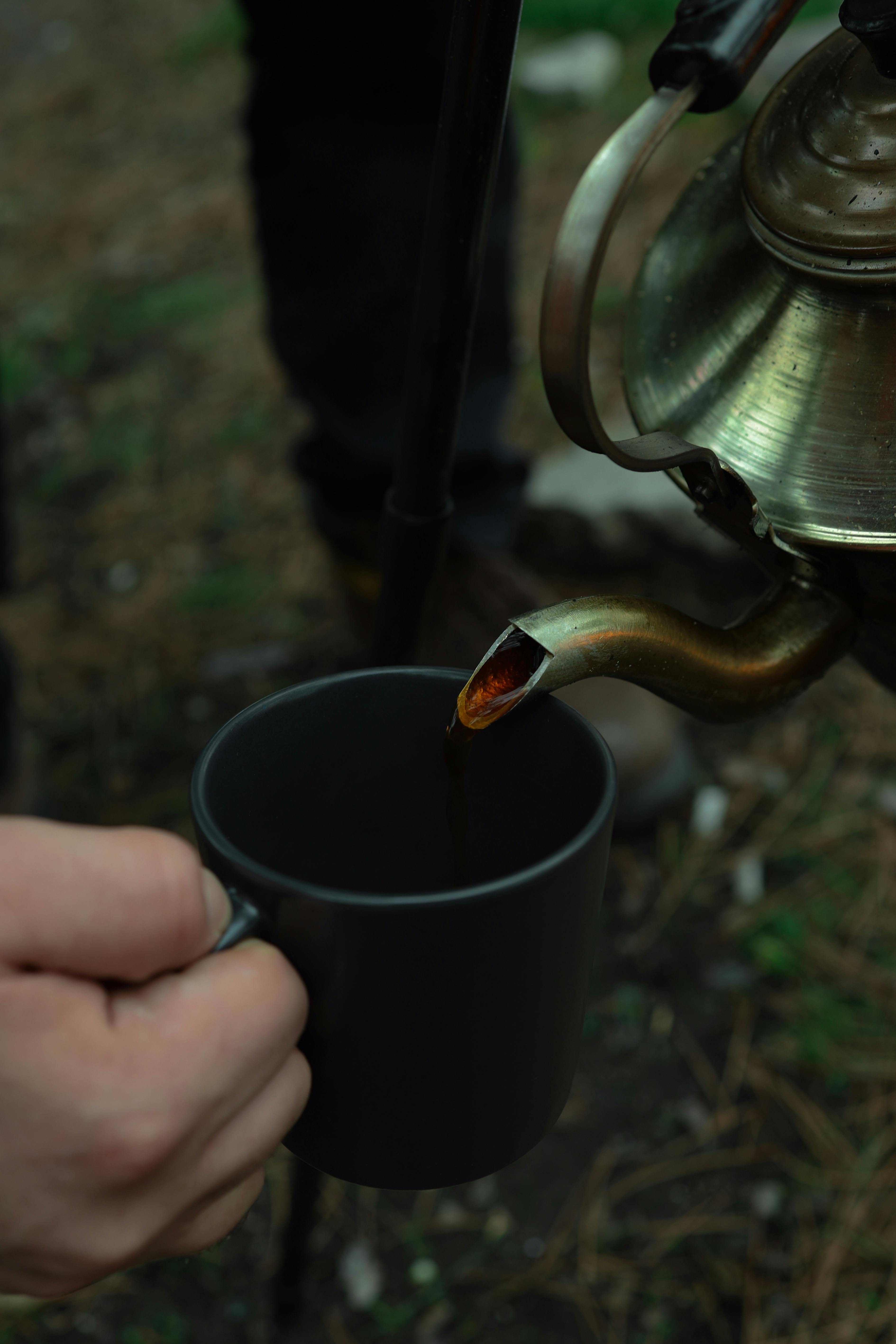 Outdoor tea being poured into a black camping mug from a kettle.