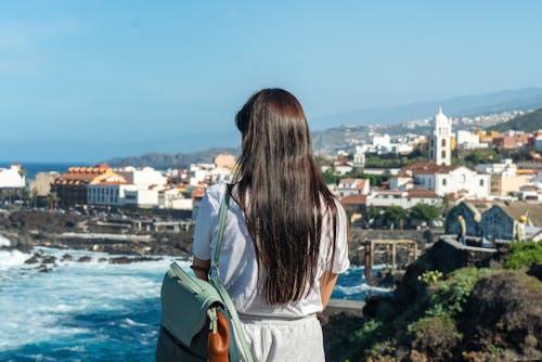 Back View of Woman with Bag Standing on Sea Shore in Town