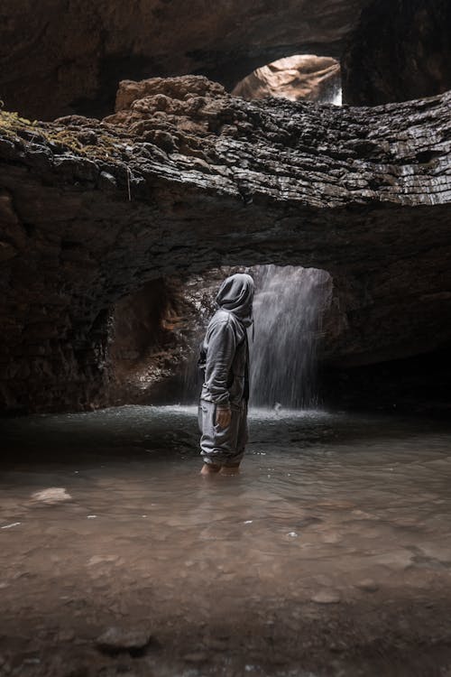 Man in Hoodie Standing in Water in Cave