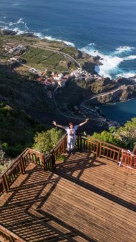 A woman stands with arms raised on a terrace overlooking Garachico, Spain's stunning coastline.
