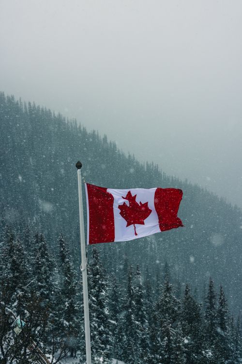 Free A dramatic scene of the Canadian flag flying in snowy weather at Banff, Alberta, showcasing patriotism and natural beauty. Stock Photo
