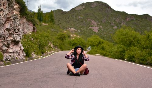 Free Woman posing on a mountain road, surrounded by greenery, wearing a black hat. Stock Photo