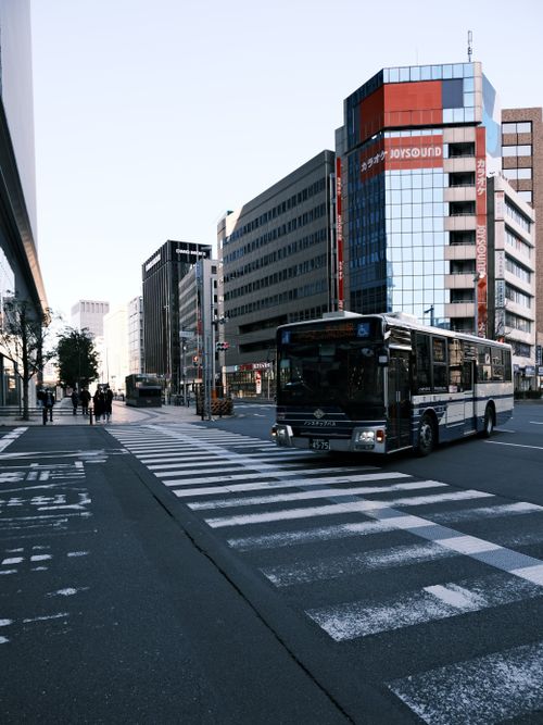 Free Public bus crossing a street in Nagoya showcasing urban architecture and vibrant city life. Stock Photo