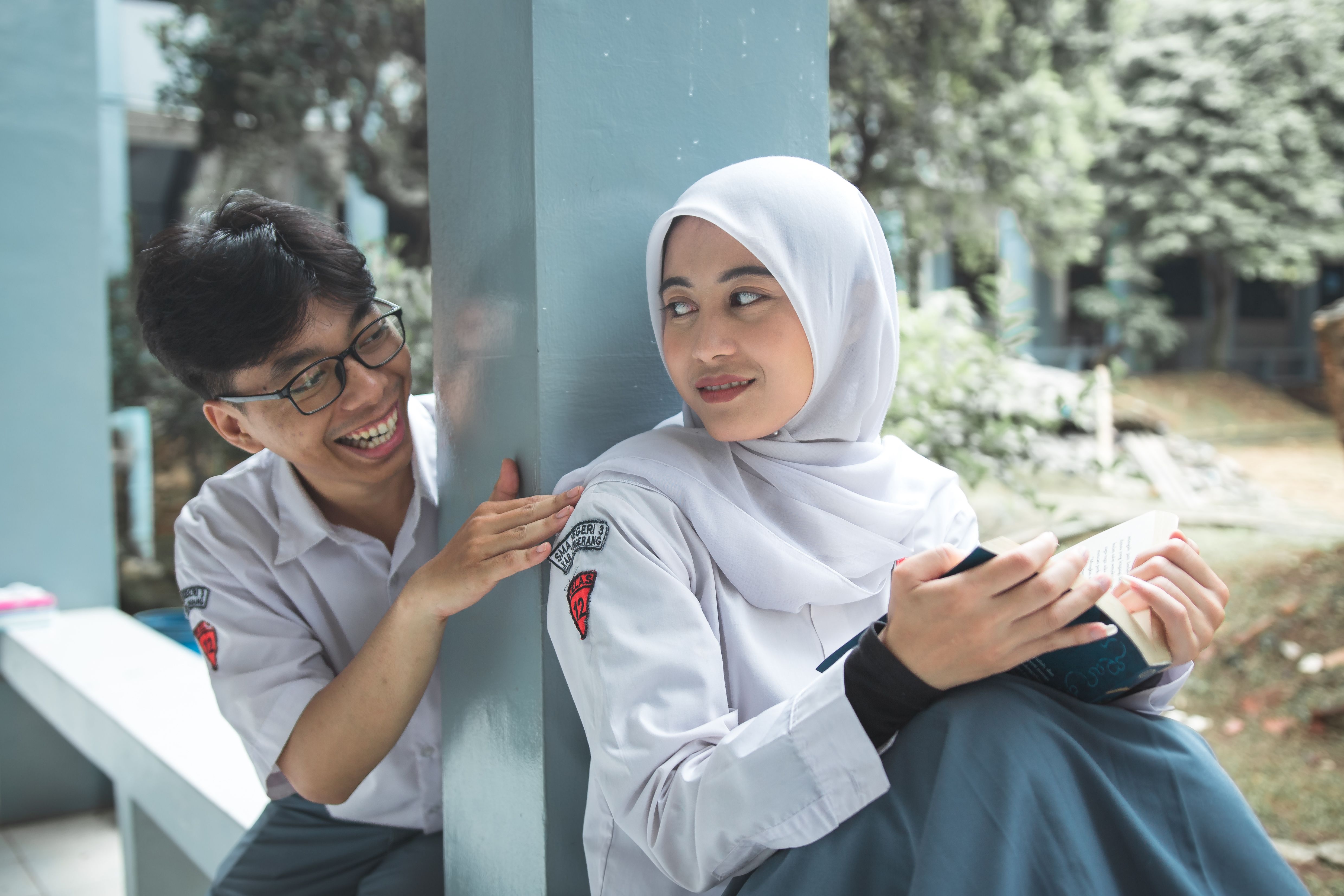 Two students sharing a light moment while studying outdoors, dressed in school uniforms.
