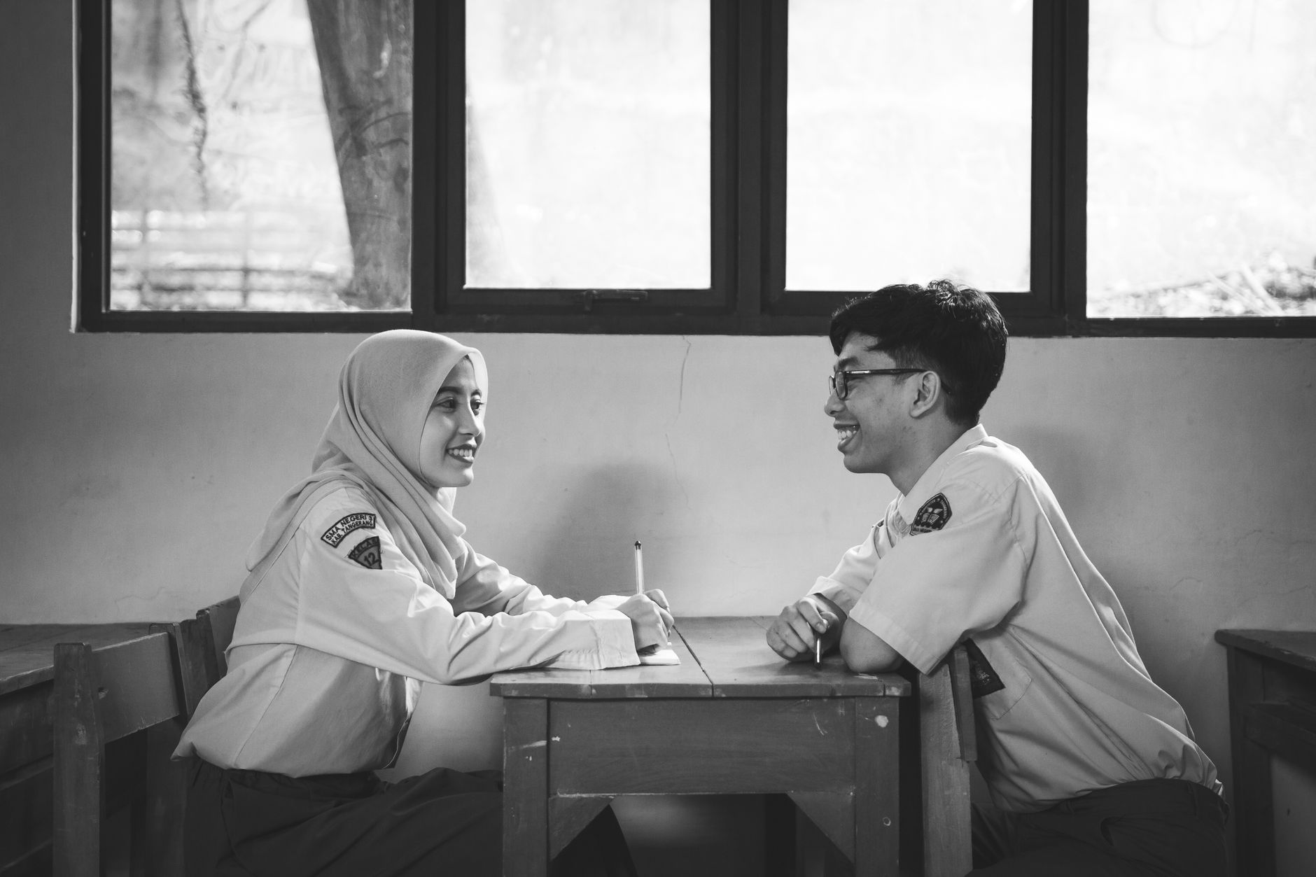 Two students in school uniforms smiling at a desk between classes.