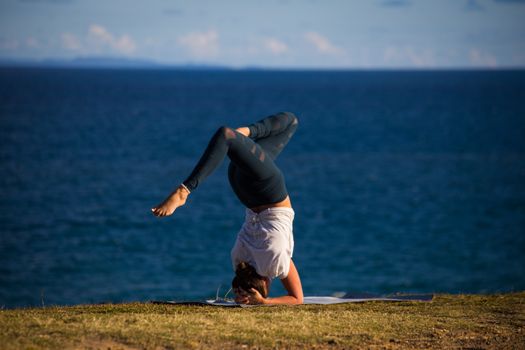 A woman performs a yoga headstand on a mat near the ocean, embracing the outdoor serenity.