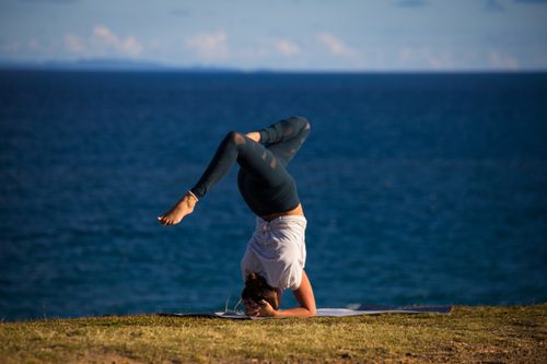 Free A woman performs a yoga headstand on a mat near the ocean, embracing the outdoor serenity. Stock Photo