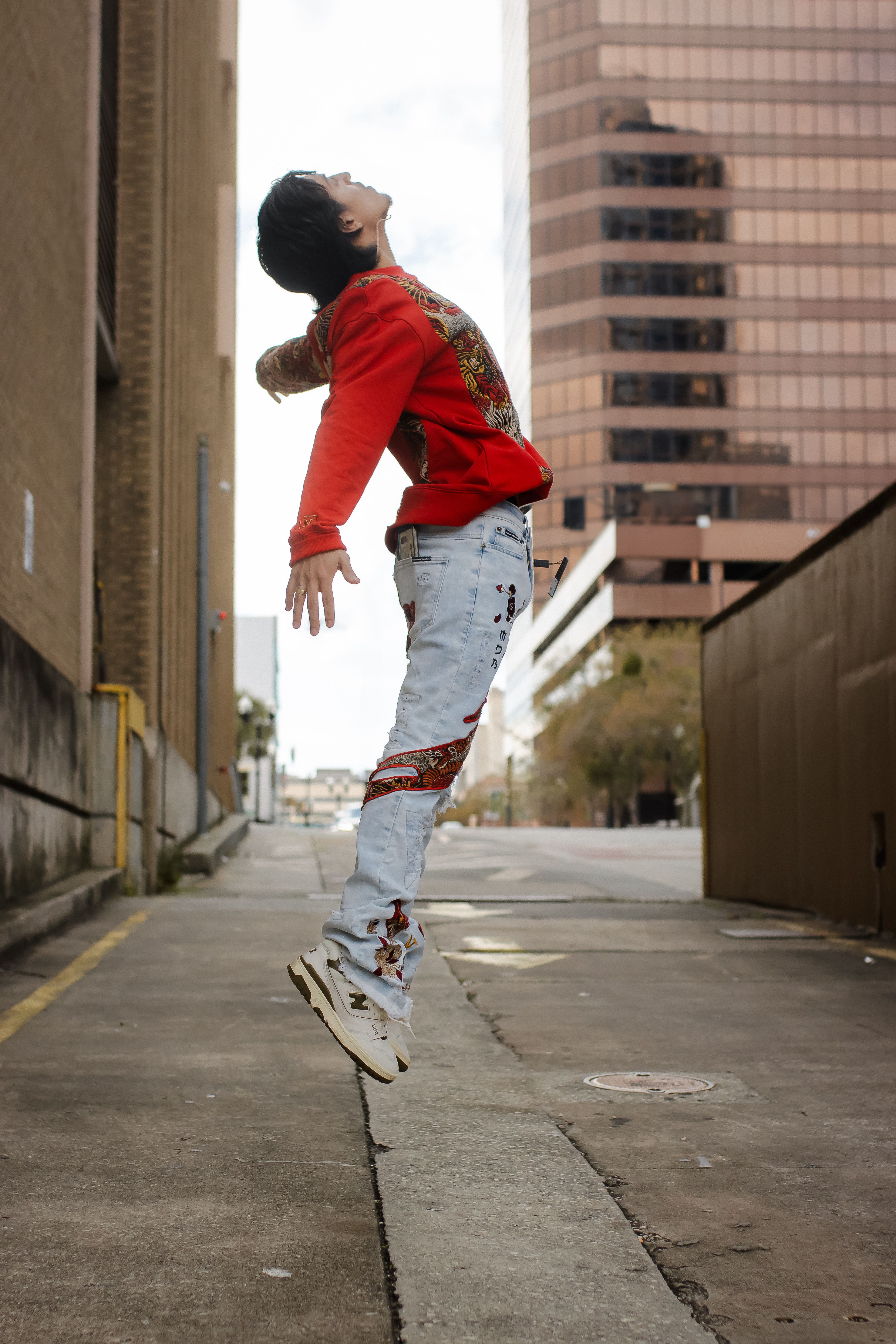 A man in a red sweatshirt and jeans jumps in an Orlando alleyway, showcasing street fashion.