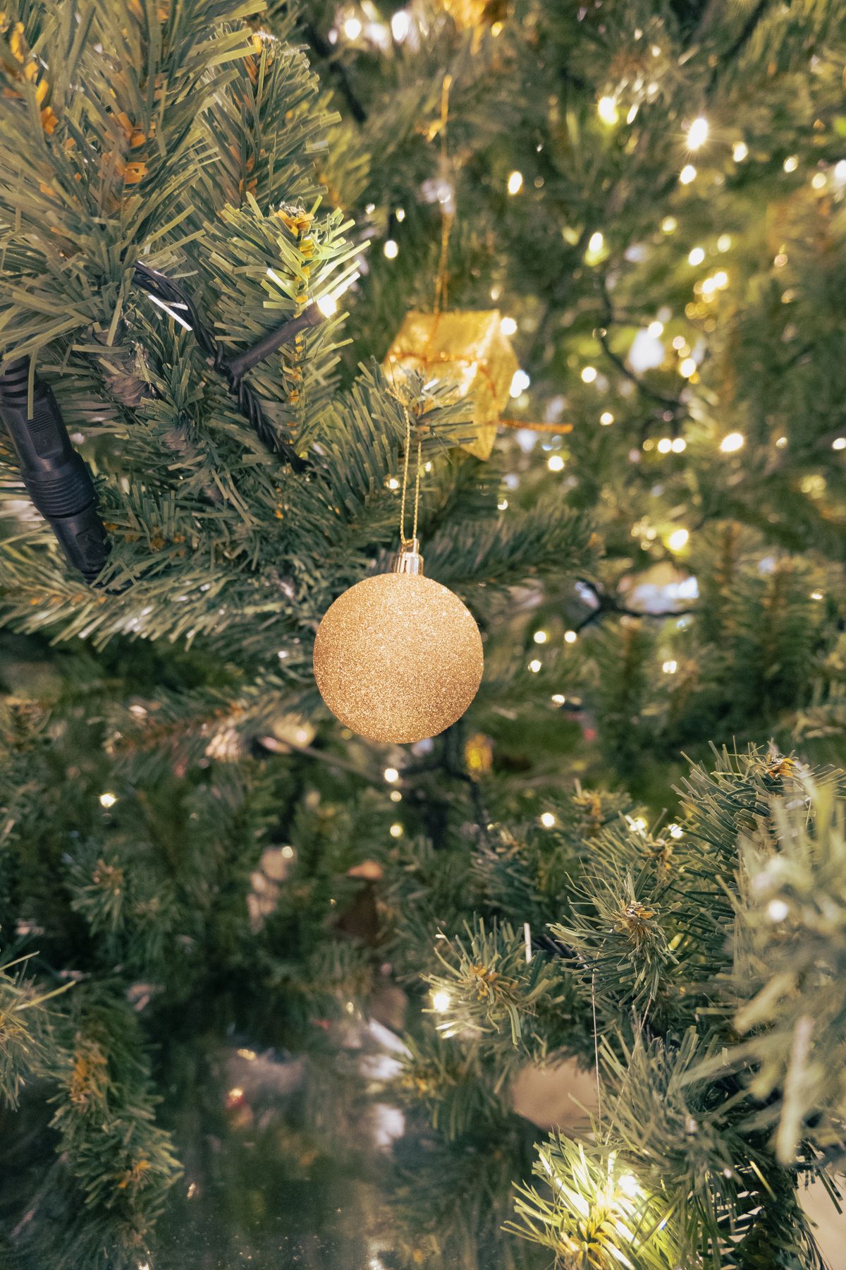 Gold bauble on a lit Christmas tree with glowing warm lights