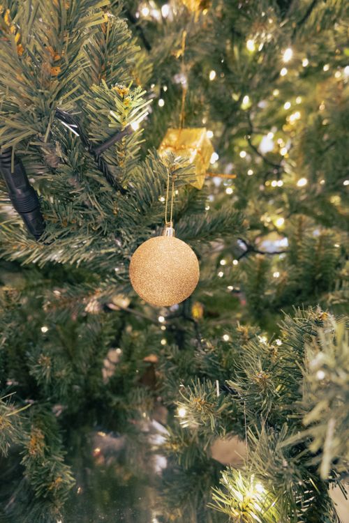 Free Close-up of a gold bauble on a beautifully lit Christmas tree with glowing lights. Stock Photo