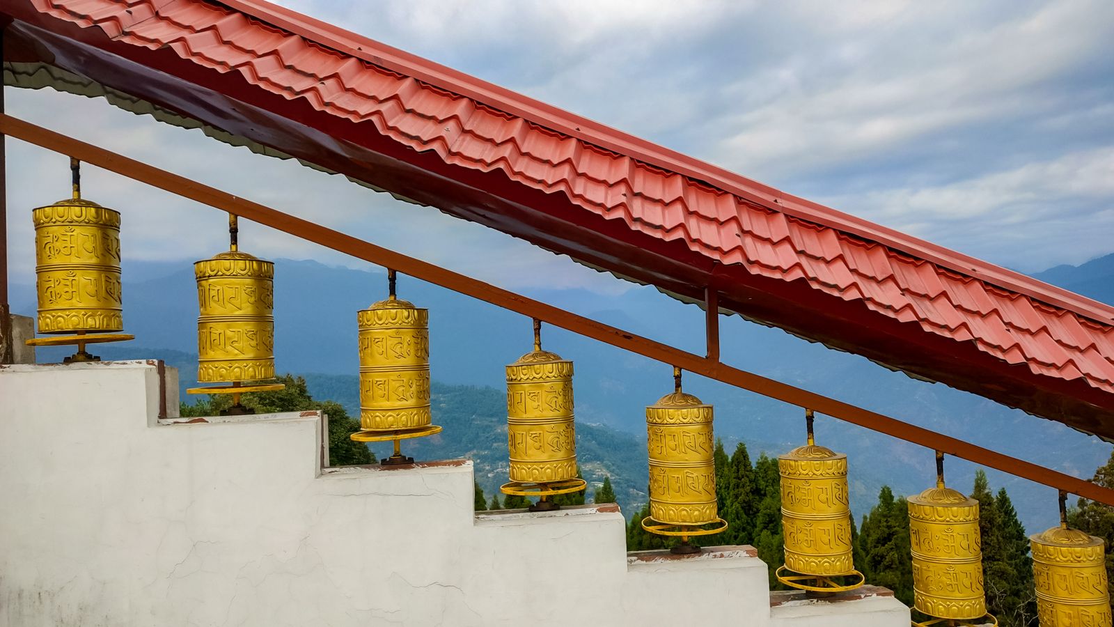 A row of golden prayer wheels on monastery steps above the wooded hills at Gangtok in Sikkim