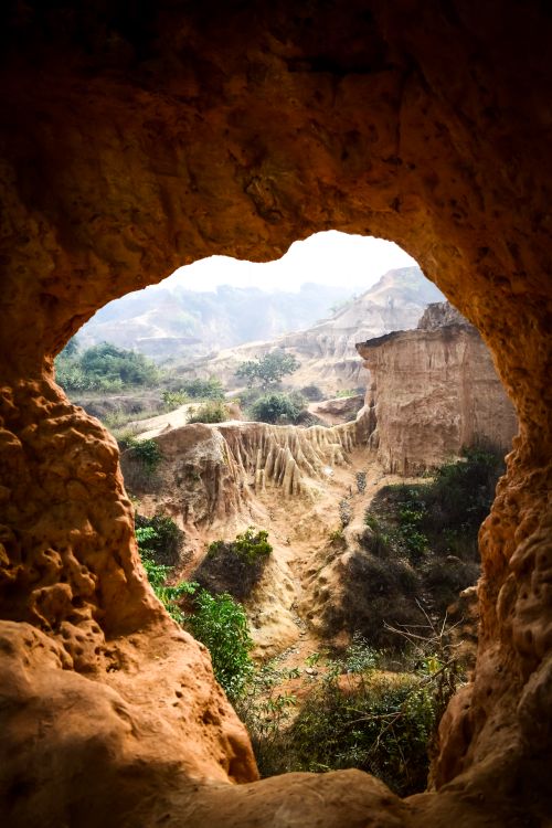 Free A breathtaking view through a cave opening into a rugged desert landscape with rock formations and greenery. Stock Photo
