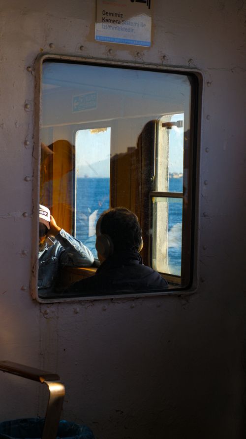 Free Passengers reflected in a window on a tranquil sea cruise, capturing serenity. Stock Photo