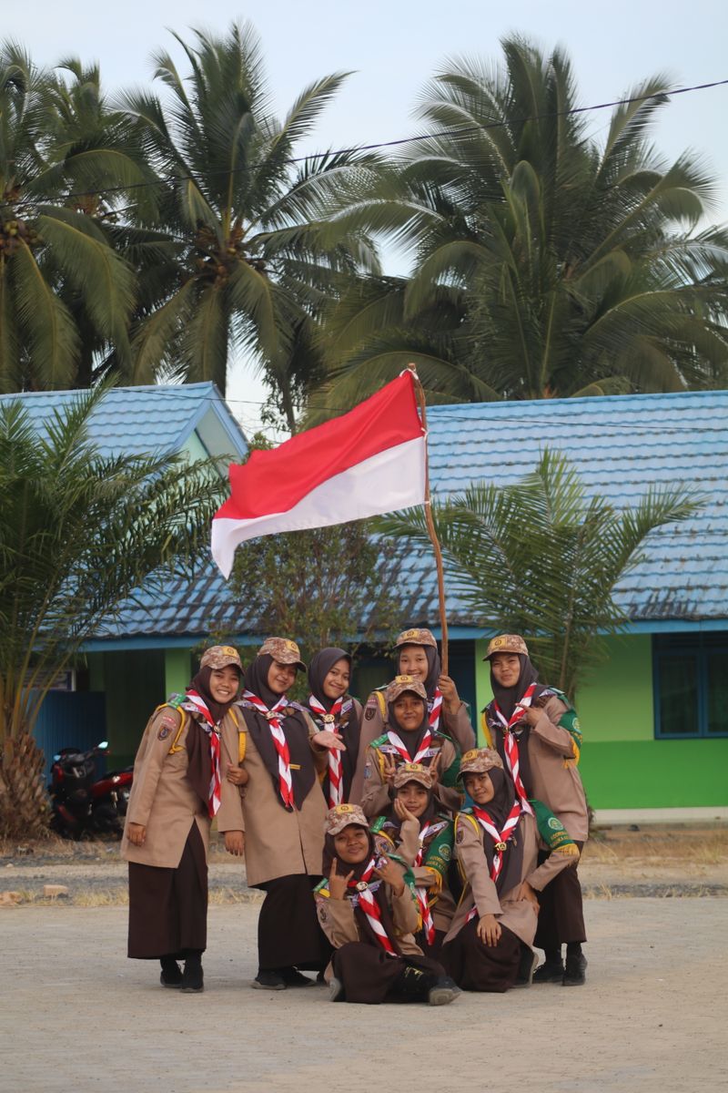 A group of scouts smiling and posing with the Indonesian flag outdoors